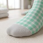 Pair of mint green and white checkerboard ankle socks with gray heel and toe panels on a white background