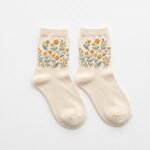 Pair of cream ankle socks with yellow floral and green leaf pattern on a white background