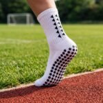 White grip sock with black non-slip dots on the sole standing on an outdoor running track