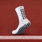 White grip sock with black non-slip dots on the sole standing on an outdoor running track