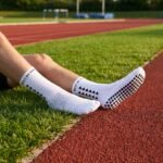 White grip sock with black non-slip dots on the sole standing on an outdoor running track