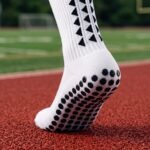 White grip sock with black non-slip dots on the sole standing on an outdoor running track