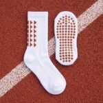White Grip Socks with brown geometric accents and non-slip sole traction dots worn on an outdoor running track