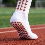 White Grip Socks with brown geometric accents and non-slip sole traction dots worn on an outdoor running track
