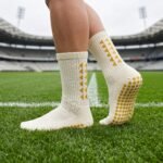 White Grip Socks with gold geometric accents and non-slip traction dots worn on a soccer field
