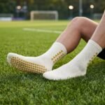White Grip Socks with gold geometric accents and non-slip traction dots worn on a soccer field