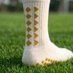 White Grip Socks with gold geometric accents and non-slip traction dots worn on a soccer field