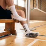 White Grip Socks with black geometric accents and anti-slip grip dots worn on an indoor sports court