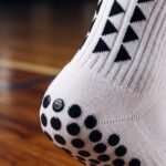 White Grip Socks with black geometric accents and anti-slip grip dots worn on an indoor sports court