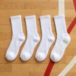 White Grip Socks with beige non-slip silicone dots on the sole, worn on an indoor sports court