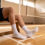 White Grip Socks with beige non-slip silicone dots on the sole, worn on an indoor sports court