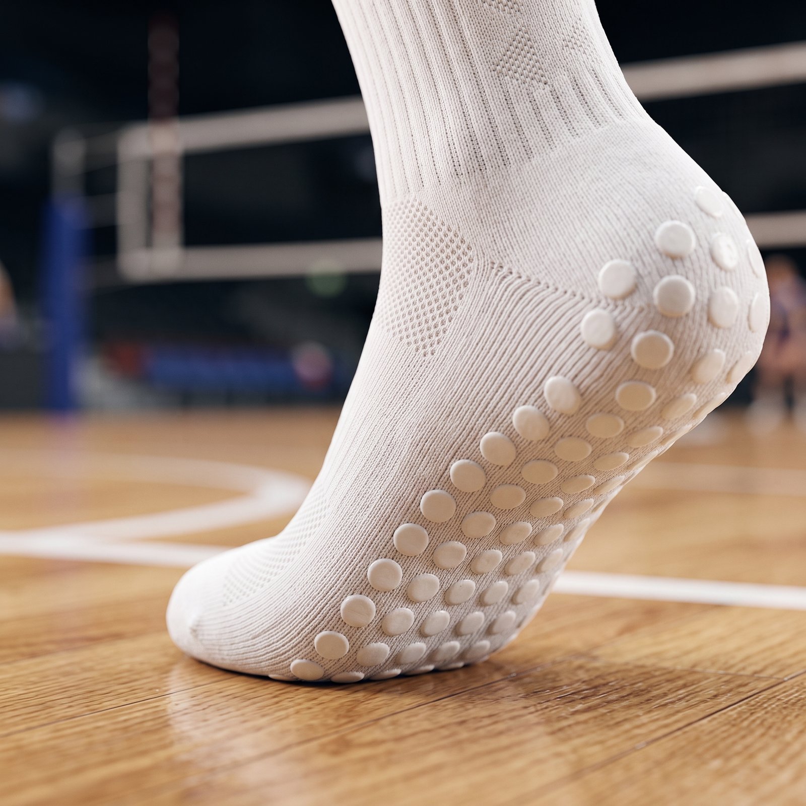 White Non-Slip Grip Socks with Silicone Traction Dots White Grip Socks with beige non-slip silicone dots on the sole, worn on an indoor sports court