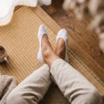 Person's foot wearing white breathable no show socks on a wooden floor, paired with dark trousers.