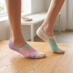 A close-up of a person's feet wearing ultra-low cut no show socks with a pastel pink, lavender, and mint green geometric pattern, standing tiptoe on a wooden surface.