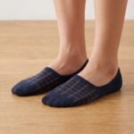 A pair of dark navy blue no show socks featuring a copper windowpane grid pattern across the top, laid flat against a clean white background.
