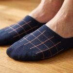 A pair of dark navy blue no show socks featuring a copper windowpane grid pattern across the top, laid flat against a clean white background.