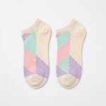 A close-up of a person's feet wearing ultra-low cut no show socks with a pastel pink, lavender, and mint green geometric pattern, standing tiptoe on a wooden surface.