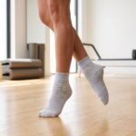 Light gray Pilates Socks with blue non-slip grip dots displayed with one sock showing the traction sole