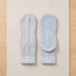 Light gray Pilates Socks with blue non-slip grip dots displayed with one sock showing the traction sole