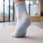 Light gray Pilates Socks with blue non-slip grip dots displayed with one sock showing the traction sole