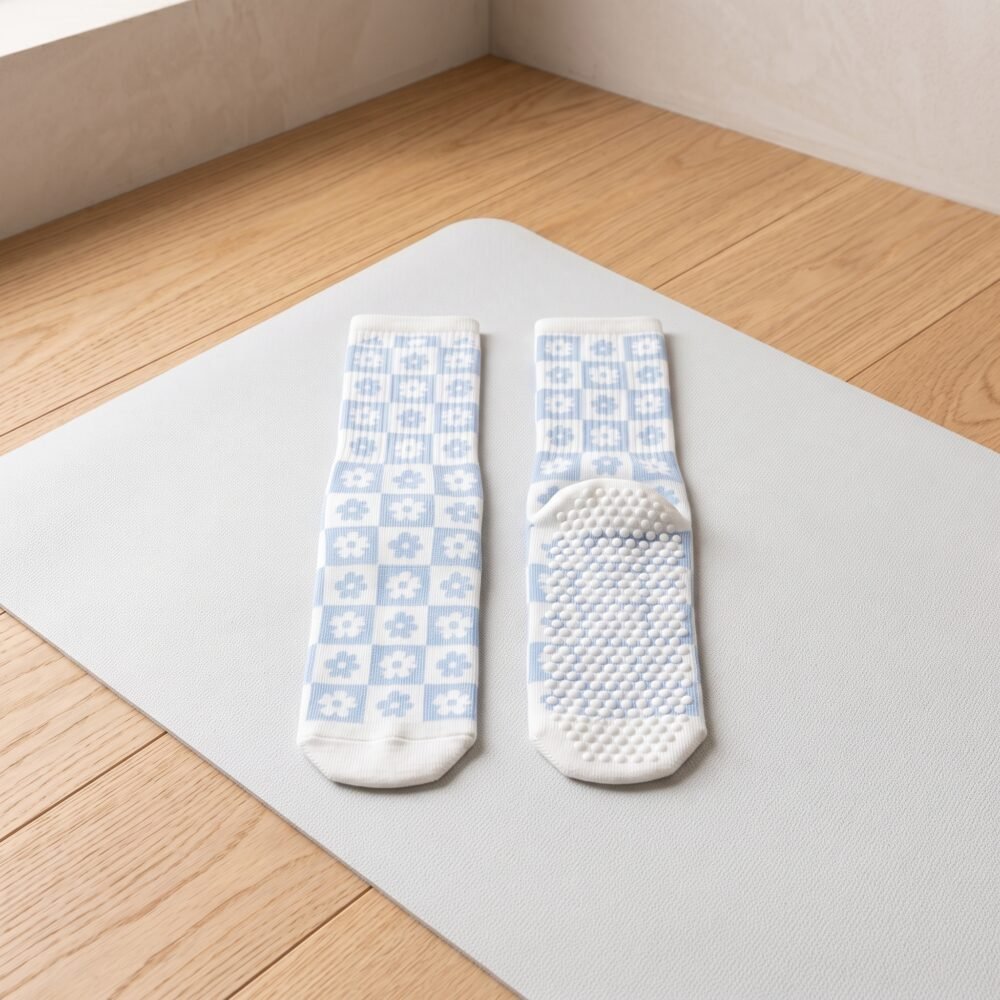 White and light blue floral pilates socks with non-slip grip soles worn on a wooden studio floor