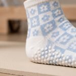 White and light blue floral pilates socks with non-slip grip soles worn on a wooden studio floor
