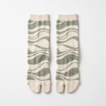 A pair of tall cream Tabi socks featuring an abstract sage green wavy pattern, laid flat against a crisp white background.