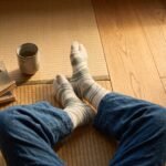 A pair of tall cream Tabi socks featuring an abstract sage green wavy pattern, laid flat against a crisp white background.
