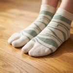 A pair of tall cream Tabi socks featuring an abstract sage green wavy pattern, laid flat against a crisp white background.