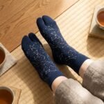 A person wearing navy blue crew-length Tabi socks featuring a gold and white star constellation pattern, standing on a light wood floor.