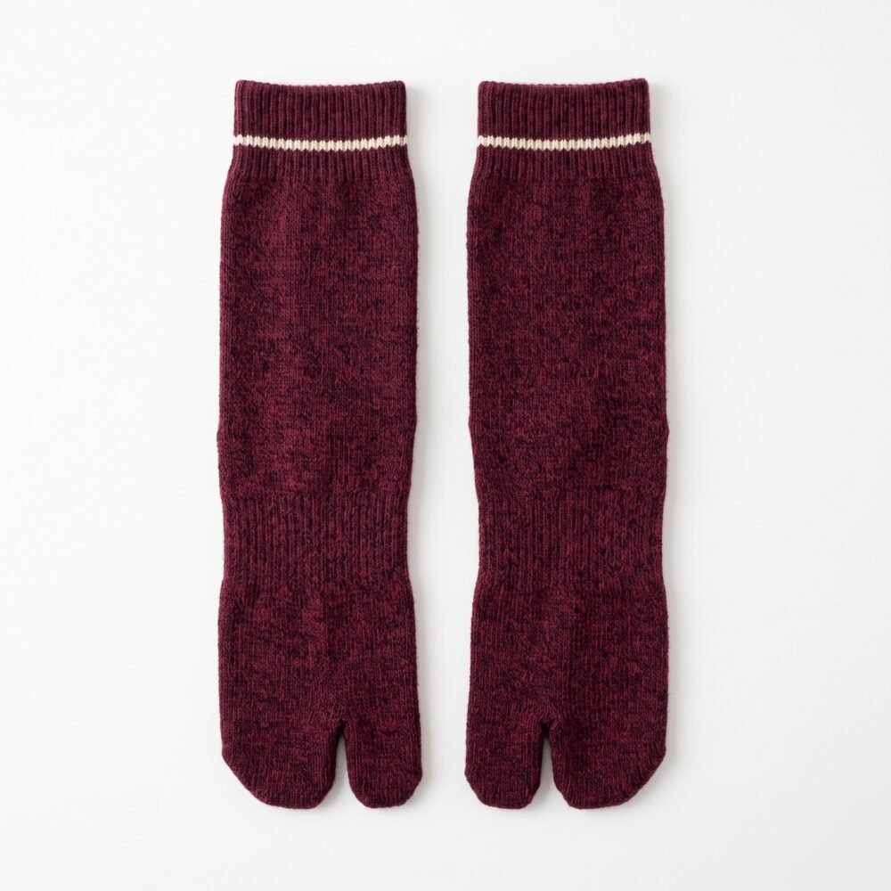 A person wearing heathered burgundy ankle-length Tabi socks with a single thin white stripe at the ribbed cuff, standing on a light wood floor.