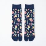 A person wearing navy blue crew-length Tabi socks featuring a colorful retro 80s geometric Memphis pattern, standing on a sunlit light wooden floor.