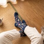 A person wearing navy blue crew-length Tabi socks featuring a colorful retro 80s geometric Memphis pattern, standing on a sunlit light wooden floor.