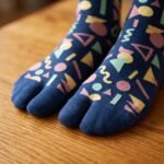 A person wearing navy blue crew-length Tabi socks featuring a colorful retro 80s geometric Memphis pattern, standing on a sunlit light wooden floor.