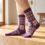 A pair of tall plum purple Tabi socks featuring a cream Nordic Fair Isle snowflake pattern, laid flat side-by-side against a crisp white background.