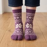 A pair of tall plum purple Tabi socks featuring a cream Nordic Fair Isle snowflake pattern, laid flat side-by-side against a crisp white background.
