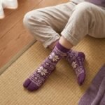 A pair of tall plum purple Tabi socks featuring a cream Nordic Fair Isle snowflake pattern, laid flat side-by-side against a crisp white background.