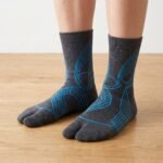 A pair of dark grey crew-length Tabi socks featuring a bright blue abstract wireframe pattern, laid flat against a crisp white background.