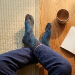 A pair of dark grey crew-length Tabi socks featuring a bright blue abstract wireframe pattern, laid flat against a crisp white background.