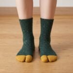 A pair of forest green speckled knit Tabi socks featuring mustard yellow toes and heels, laid flat against a clean white background.