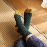 A pair of forest green speckled knit Tabi socks featuring mustard yellow toes and heels, laid flat against a clean white background.