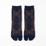 A person wearing navy blue crew-length Tabi socks featuring a copper geometric line pattern, standing on a light wood floor.