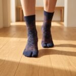 A person wearing navy blue crew-length Tabi socks featuring a copper geometric line pattern, standing on a light wood floor.