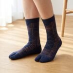 A person wearing navy blue crew-length Tabi socks featuring a copper geometric line pattern, standing on a light wood floor.
