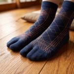 A person wearing navy blue crew-length Tabi socks featuring a copper geometric line pattern, standing on a light wood floor.